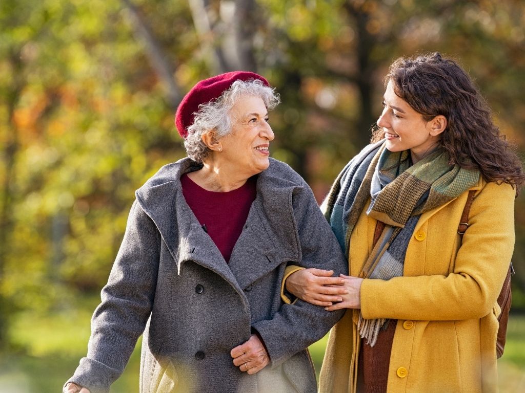 Caregiver walking with an elderly woman Caregiver walking arm-in-arm with an elderly woman on a sidewalk, providing steadying support.