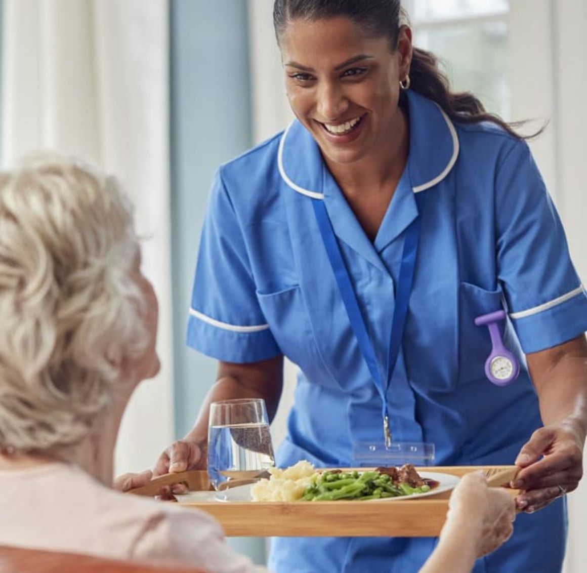 Caregiver handing a tray of food to an elderly lady meal preparation